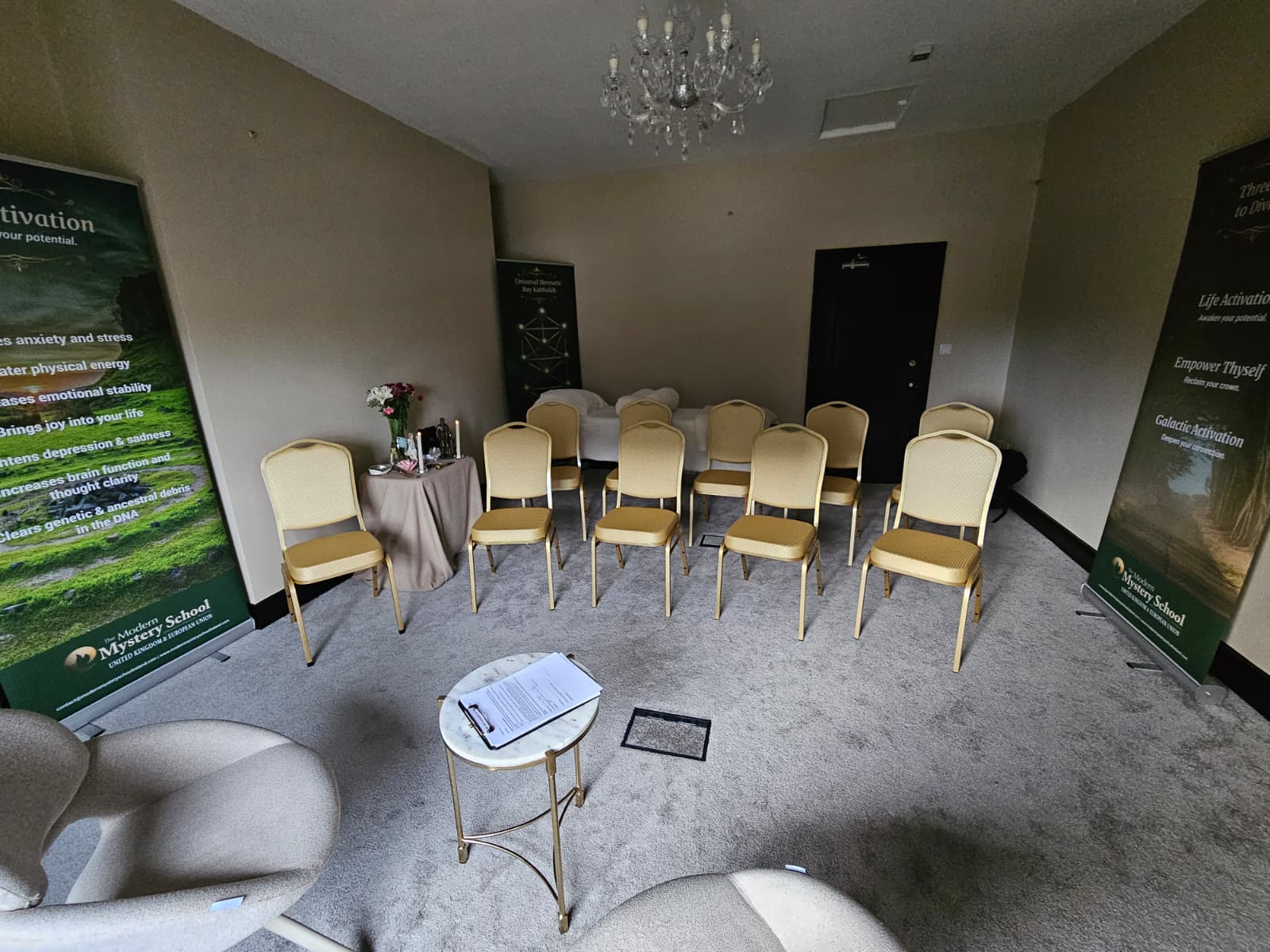 Èriu teaching room arranged with chairs, a table, chandelier, and Modern Mystery School banners